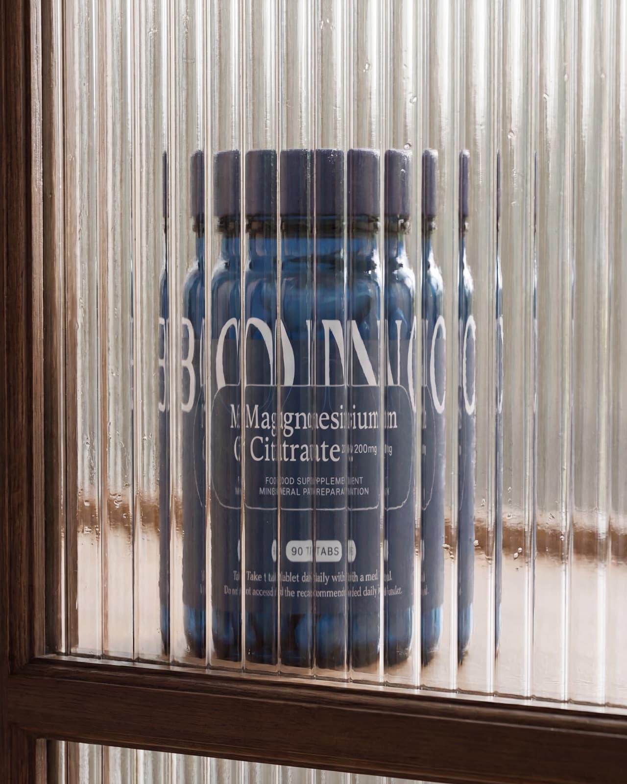 Un pot de BONO Supplements Citrate de magnésium derrière du verre cannelé